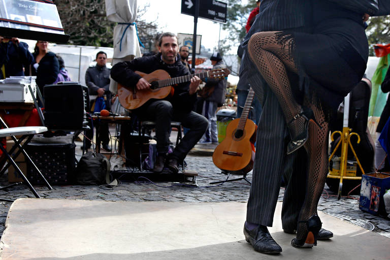 Casal dança tango enquanto artista de rua toca música na feira de San Telmo