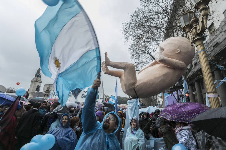 Bebê gigante é carregado por pessoas com roupas azuis e bandeiras da Argentina