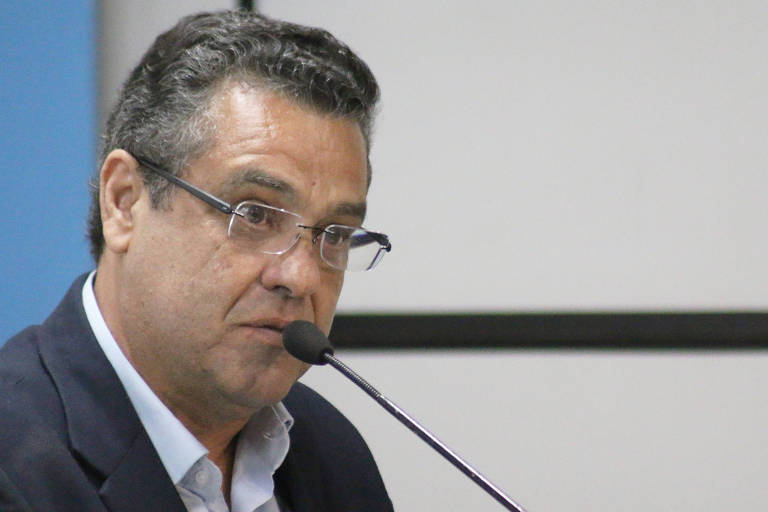 Marcelo Barbieri, de óculos, fala em um microfone