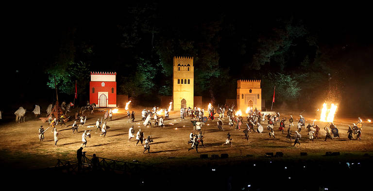 Encenação de combate medieval à noite em um campo, com tochas de fogo acesas