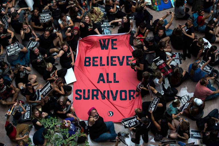 Grupo de cerca de 50 pessoas veste de preto e carrega uma faixa vermelha com a frase: "Nós acreditamos em todos os sobreviventes"