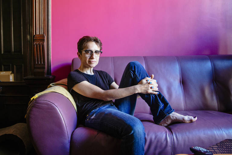 Escritora Masha Gessen sentada em um sofá roxo, encontrada em uma parede pink