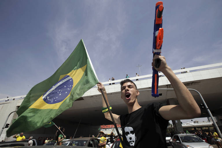 Apoiador de Jair Bolsonaro (PSL) segura arma de brinquedo e bandeira do Brasil durante carreata em Brasília
