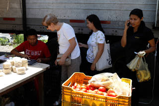 A vendor uses a point-of-sale (POS) device as people wait in line at a vegetable and fruit stall at a street market in Caracas