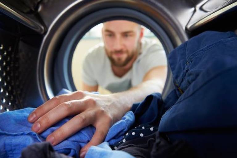 Homem mexe com roupas na máquina de lavar