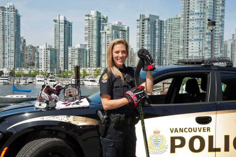 A atleta Meghan Agosta posa para foto de uniforme de policial e luvas de hóquei com a cidade de Vancouver ao fundo 