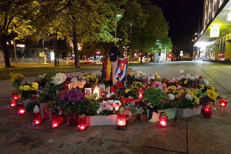 Memorial tem flores, sequência de velas e as bandeiras da Alemanha e de Cuba