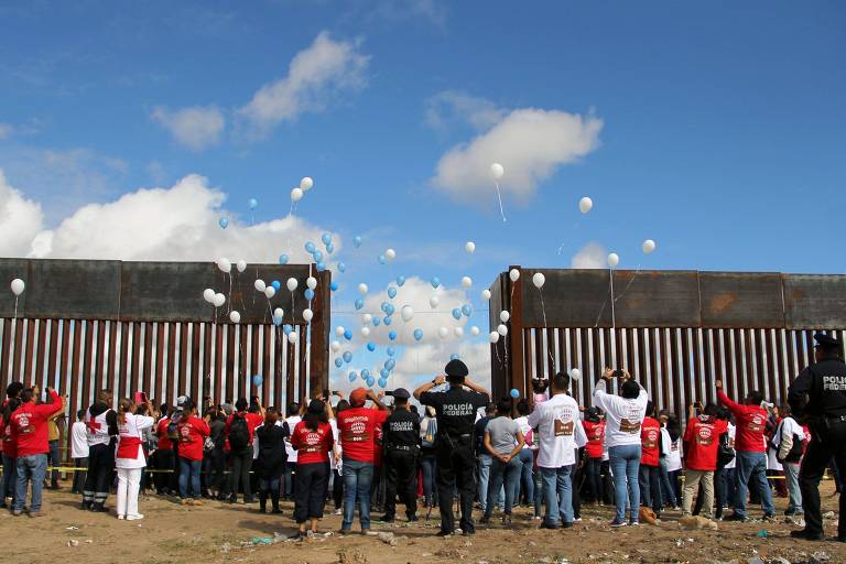 Grupo solta balões perto de grade de fronteira