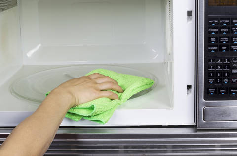 Hand with microfiber cleaning rag wiping inside of microwave oven. Credit Tom Baker / Fotolia