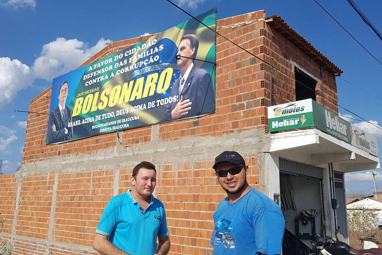 Luis Carlos da Silva Mota (esquerda) e Jango Beltiman, eleitores de Bolsonaro na cidade de Irauçuba (CE), com o outdoor colocado por comerciantes da cidade