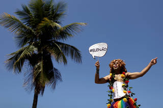 A reveler taking part in the Gay Pride Parade at Copacabana beach holds a sign against presidential candidate Bolsonaro in Rio de Janeiro