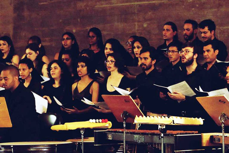 Membros do coro da Escola Municipal de Música de São Paulo ensaiam de pé, com partituras na mão  