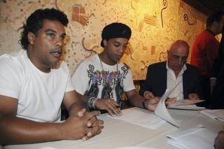 Brazilian soccer player Ronaldinho, his brother Roberto Assis and AC Milan's Vice President Adriano Galliani check the contract with Brazil soccer team Flamengo in a restaurant in Rio de Janeiro