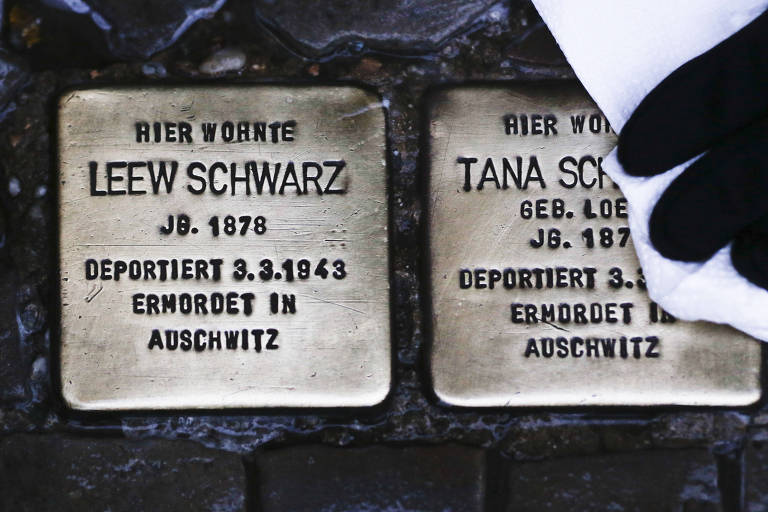 Homem pole placas que lembram a morte de duas vítimas do Holocausto capturadas na Noite dos Cristais em Berlim