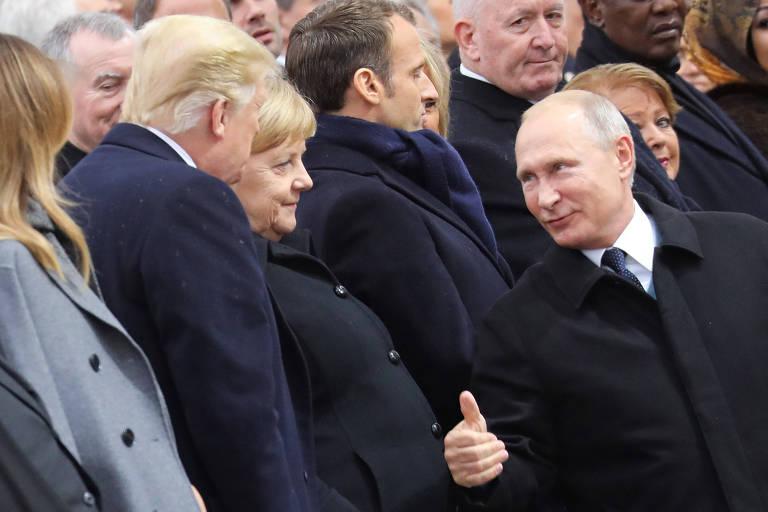 Trump aparece de perfil em uma fila de líderes, ao lado de Merkel e do presidente francês, Emmanuel Macron. Putin passa ao lado deles.