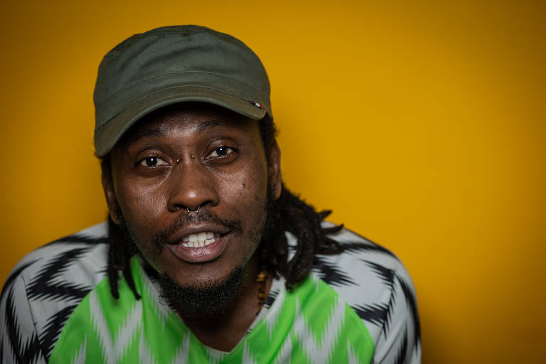 De boné e com camisa verde e branca da seleção nigeriana, rapper Rincon Sapiência posa para foto 