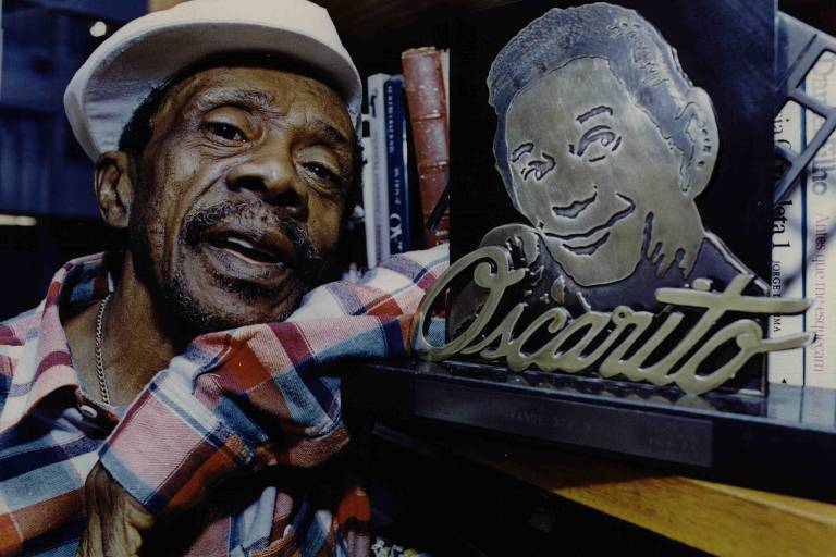 O ator Grande Otelo posa ao lado de imagem de Oscarito, em sua casa no Rio