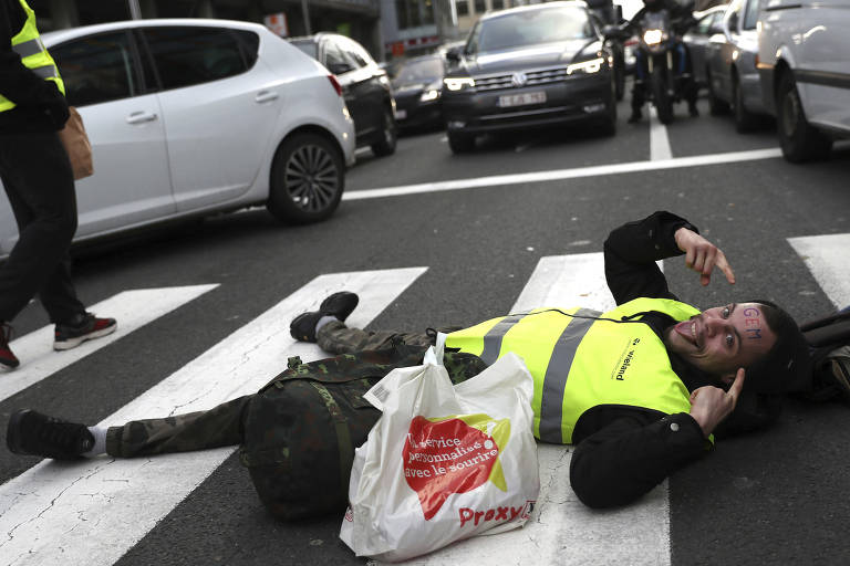 Manifestante usando colete amarelo deita em rua para bloquear o tráfego durante ato em Bruxelas, na Bélgica, contra o alto preço dos combustíveis