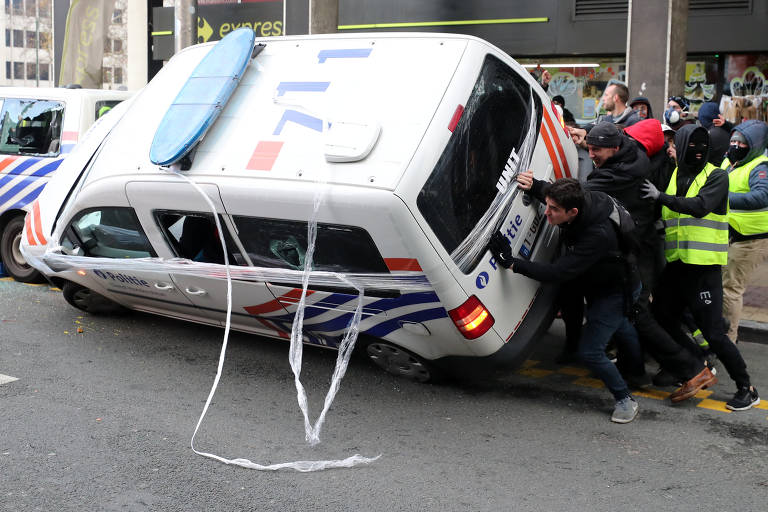 Manifestantes mascarados viram viatura policial durante ato em Bruxelas, na Bélgica, contra alta do preço dos combustíveis