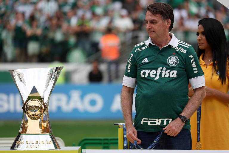 No Allianz Parque, em São Paulo, o presidente Jair Bolsonaro, vestido com camisa do Palmeiras, observa o troféu do Campeonato Brasileiro