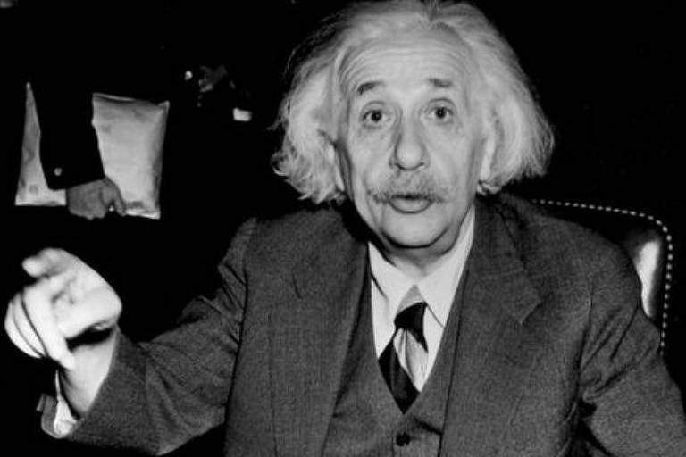 Einstein olha para a câmera e levanta a mão, apontando com um dedo