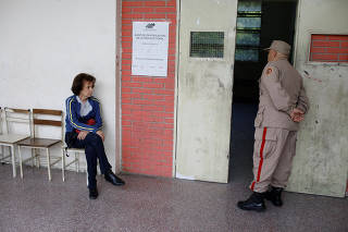 A woman waits to vote as a militia member stands guard at a polling station during the municipal legislators election in Caracas
