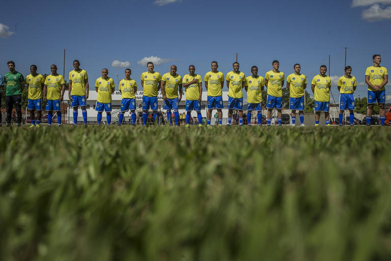Jogadores em fila, com calção azul e camiseta amarela, em gramado 