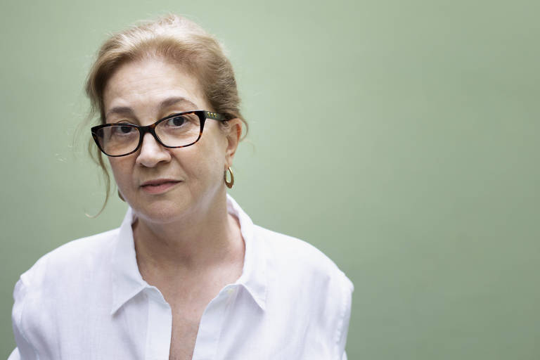 Leda Spinardi, a Ledusha, é uma mulher de 65 anos, com os cabelos tingidos de louro castanho, usa óculos e camisa branca; sua expressão é de um meio sorriso, o fundo da foto é verde