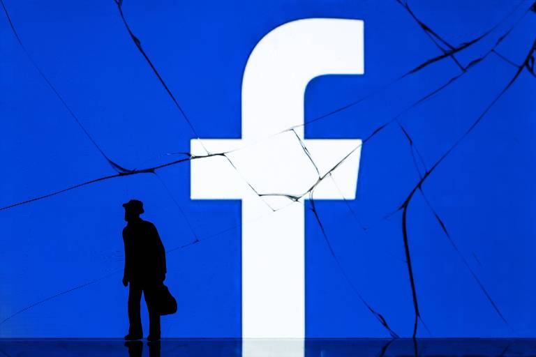 Homem em frente à logomarca do Facebook exibida em telão em Paris