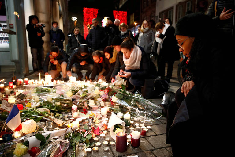 pessoas colocam flores e velas em homenagem aos mortos do atentado na frança