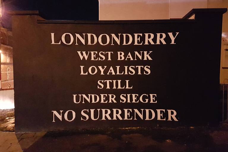 Muro com a inscrição "Legalistas da margem oeste de Londonderry ainda sitiados. Sem rendição", em zona da cidade que costumava concentrar protestantes unionistas (pró-Reino Unido)