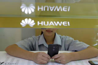 FILE PHOTO: A sales assistant looks at her mobile phone as she waits for customers behind a counter at a Huawei booth in Wuhan