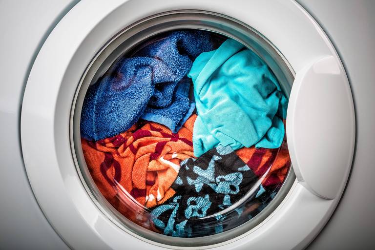 Roupas coloridas em lavagem em uma máquina de lavar que tem porta redonda e frontal