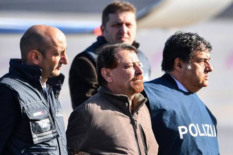 Italian former communist militant Cesare Battisti (C), wanted in Rome for four murders attributed to a far-left group in the 1970s, is escorted by Italian Police officers after stepping off a plane coming from Bolivia and chartered by Italian authorities, after landing at Ciampino airport in Rome on January 14, 2019. - Former communist militant Cesare Battisti landed in Rome on January 14 after an international police squad tracked the Italian down and arrested him in Bolivia, ending almost four decades on the run. (Photo by Alberto PIZZOLI / AFP)
