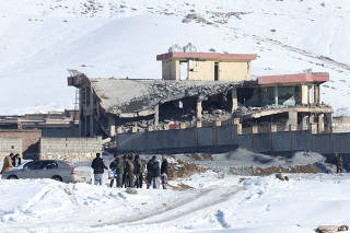 Afghan men stand in front of a collapsed building of a military base after a car bomb attack in Maidan Wardak