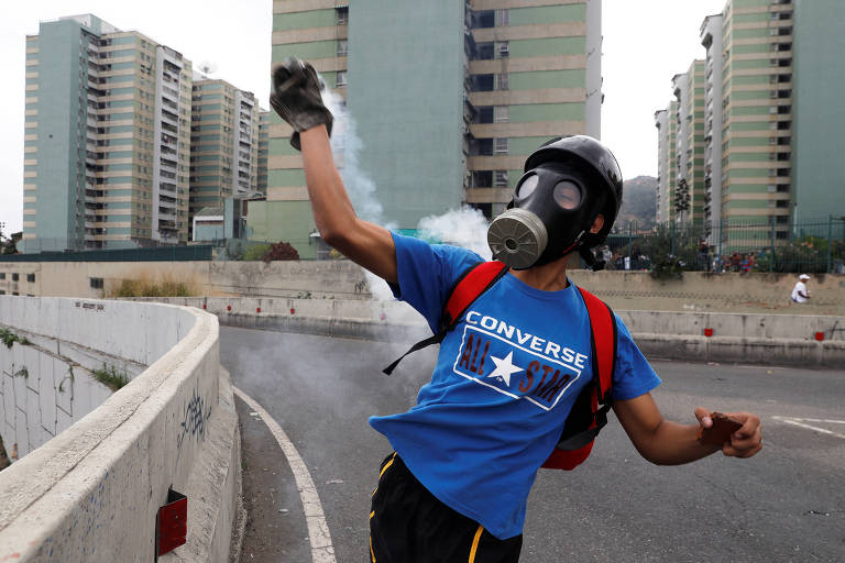 Manifestante arremessa bomba de gás lacrimogêneo durante o protesto em Caracas 