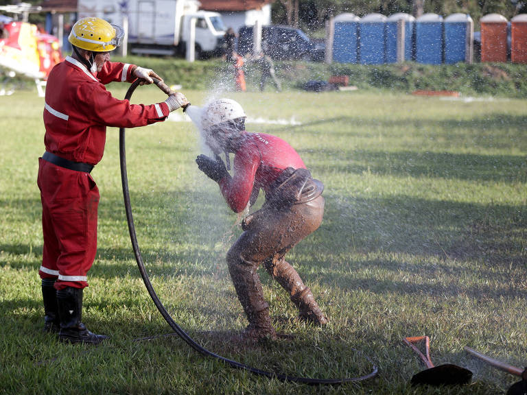 Bombeiros que estavam fazendo resgate na lama se lavam com mangueira depois do trabalho de busca e resgate de desaparecidos na região de Brumadinho (MG)