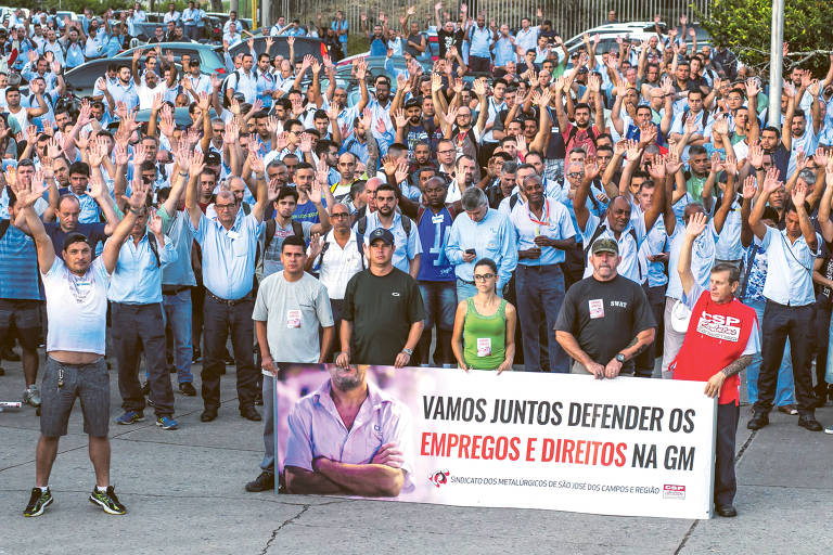 Trabalhadores da GM, em pé, com as mãos para o auto e com faixas de protesto, em São José dos Campos se manifestam  contra proposta de reestruturação da montadora, no dia 1º de fevereiro