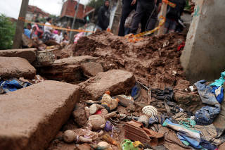 Residents look at a house damaged in a mudslide after heavy rains in Maua