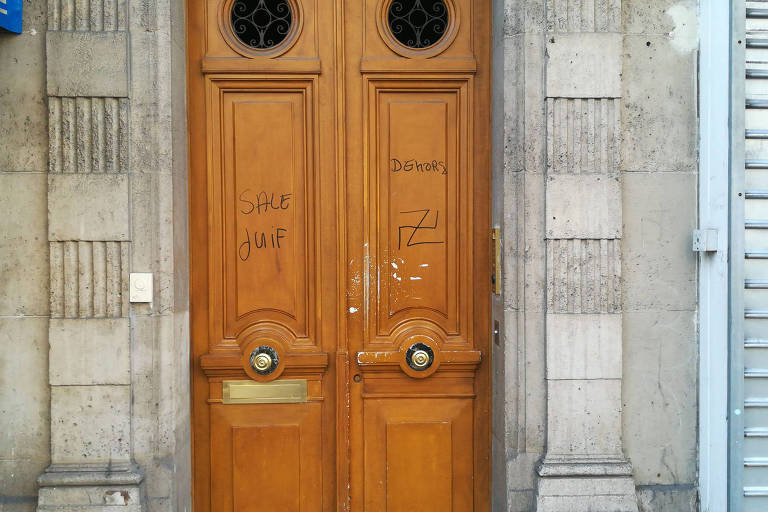 Porta de edifício em Paris com a pichação "judeu sujo, saia" e uma suástica