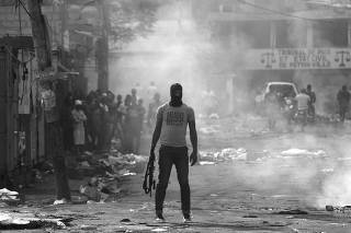 A man holds a weapon next to burning barricades during anti-government protests in Port-au-Prince