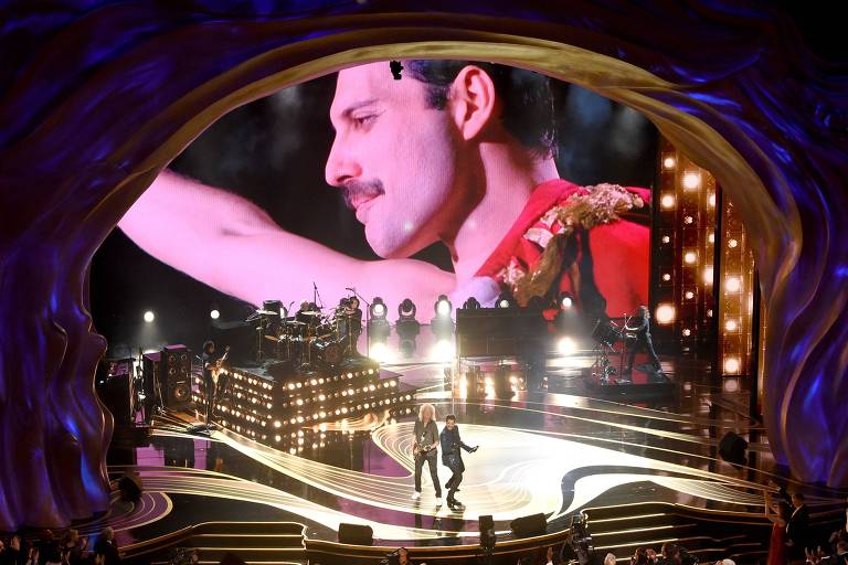 Foto da Banda Queen no Oscar, com uma projeção de Freddie Mercury