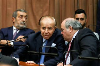 FILE PHOTO: Former Argentine President Carlos Menem talks to an unidentified man behind former prosecutor Eamon Mullen in a court room before hearing the verdict in the trial of covering up the 1994 AMIA bombing, in Buenos Aires