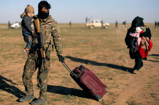 A fighter from Syrian Democratic Forces (SDF) holds a baby near the village of Baghouz, Deir Al Zor province