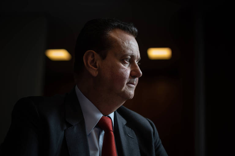 Usando um terno escuro e gravata vermelha, o presidente nacional do PSD, Gilberto Kassab, concede entrevista em uma sala escura