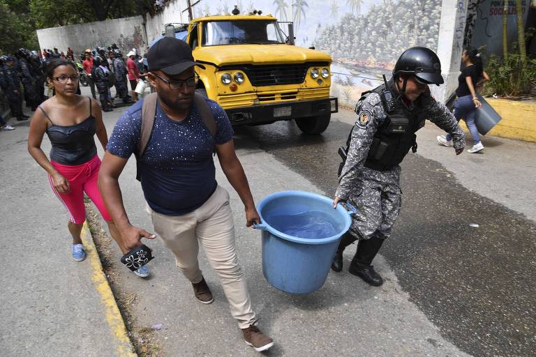 Policial ajuda homem a carregar balde com água no bairro de San Agustín, em Caracas 