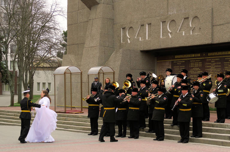 Em frente a monumento a mortos na Segunda Guerra, noiva e sargento da Marinha Russa dançam ao som de uma banda militar, tradição local