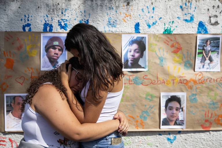 Estudantes se abraçam em frente a cartaz com fotos das vítimas do massacre em Suzano
