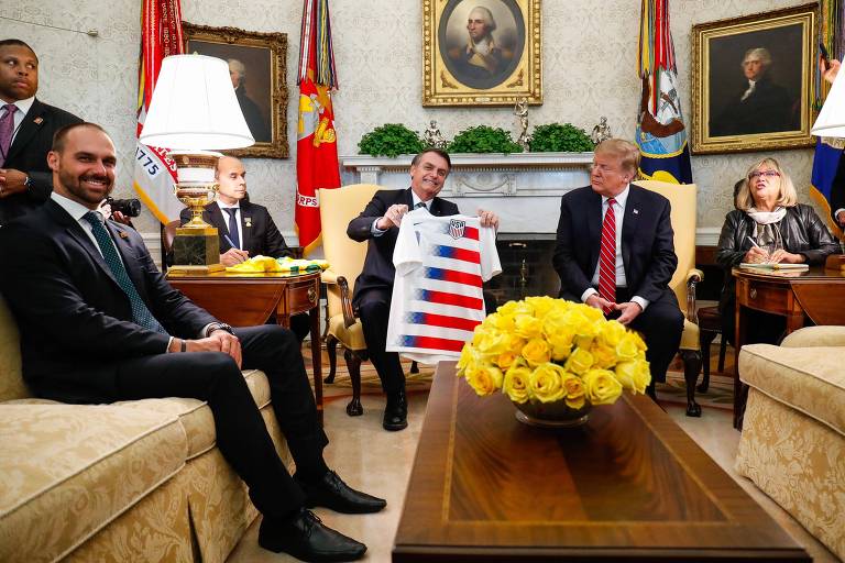 Bolsonaro com camisa que ganhou de Trump, em encontro na Casa Branca com a presença de Eduardo (esq.)