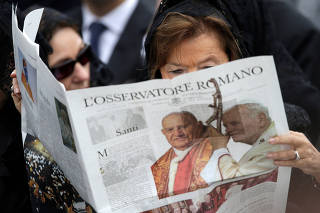 FILE PHOTO: A woman reads a copy of the Vatican newspaper L'Osservatore Romano as she waits for the canonisation ceremony in St Peter's Square at the Vatican